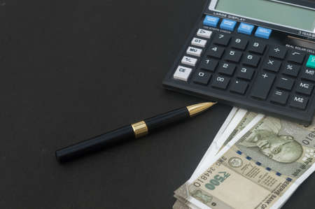 Indian Rupee placed near calculator and a pen on table. Isolated on black background.の写真素材