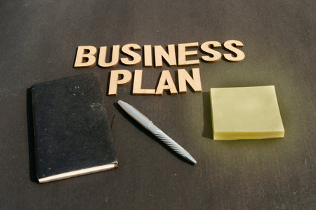 Businessman hand placing a pen and notebook in front of Word Business Plan made of wooden blocks of Alphabet letters. High Angle View. Vertical background. Close upの写真素材