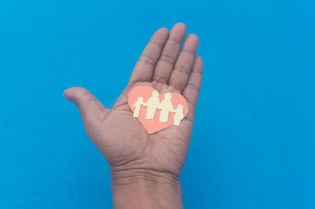Happy paper family on a man hand with palm facing upwards against blue background. Origami Papercraft decorative shapes and figures.の写真素材