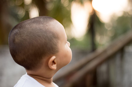 Close up Adorable baby boy in the evening sunlight looking at the Sunset sky. Little child at outdoors. Kid exploring nature. Hope concept. Rear View.の写真素材