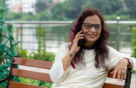 Smiling Woman with long brown hair Speaking on mobile phone relaxing outdoors. Closeup. She is wearing White T-shirt and specs. Front view. Head and Shoulder Shot.の写真素材