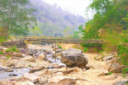 Large Boulder Rocks and river streams flowing in a mountain valley against hill, forest, and a Bamboo bridge in the background. Rangbang river mountain valley. Tabakoshi West Bengal Indiaの写真素材