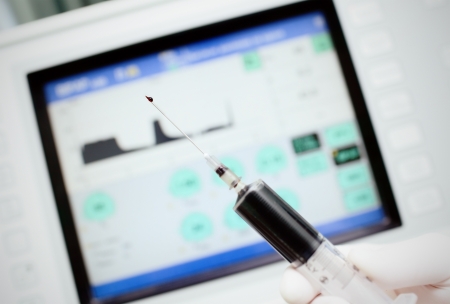 Drop on the tip of the medical needle  Syringe with medicine in hand on a background of the monitor の写真素材