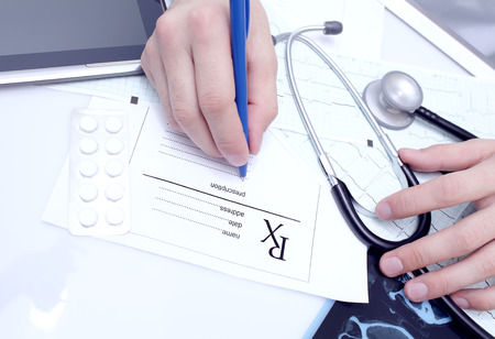 Doctor writes a prescription at his desk の写真素材