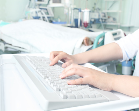 Doctor at the computer typing in ward of patientの写真素材