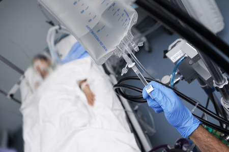 Male person with gloved hand turns off the intravenous drug system to the unconscious patient.の写真素材