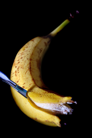 Cutting banana with the surgical knife on the black background.の写真素材