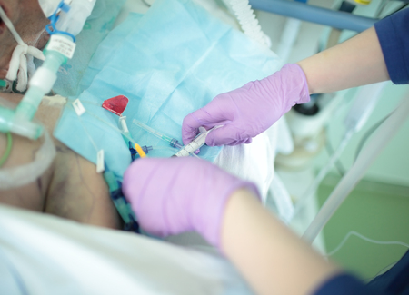 Nurse injects a drug into the catheter of an elderly patient in a coma.の写真素材