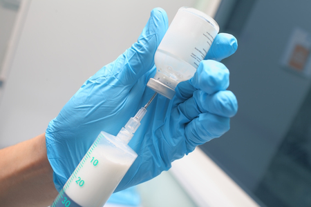 Male doctor in the blue gloves filling the syringe with white drug for injection.の写真素材
