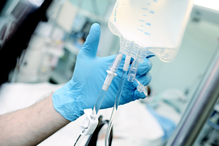 Male medical worker regulate the intravenous drip system at the patient bed in the critical care unit.の写真素材