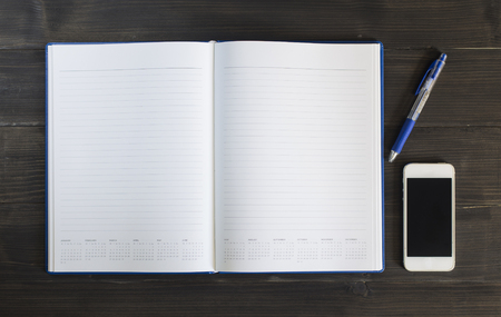 Note book with pen and smart phone on the wooden background.の写真素材