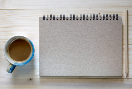 A Notebook with a pencil and coffee cup on wooden background.の写真素材
