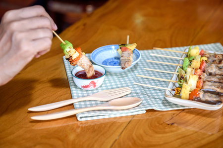 Closed up of girl is eating pork Bar B Que(BBQ) with vegetable(Bell pepper,tomato,pineapple) and tomato sauceの写真素材