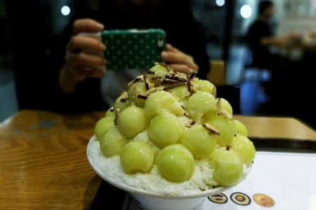 women taking photo of sweet melon bingsu dessert with smart phone.の写真素材