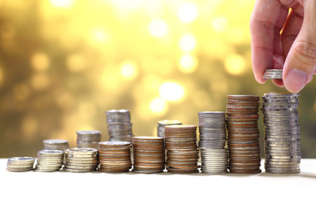 Coin stack row hand holding coin making a tower. Yellow gold circular light background.