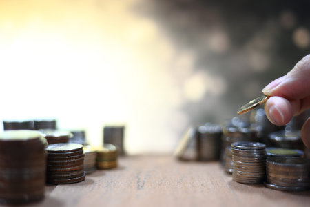 hand holding and arranging coin into stacking pile column on lighting bokeh background
