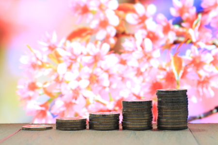 Environmental friendly economy. Finance business of saving nature. Coin pile stacked in increasing chart shape on wood board with out of focus pink flower background.の写真素材