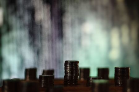 big coin piles in front of out of focus computer screen displayed blue green code matrix. online saving innovation idea.の写真素材