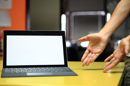 business presentation on screen. mock up blank laptop monitor display for copy space. notebook on table and hands pointing toward in an inviting position.の写真素材