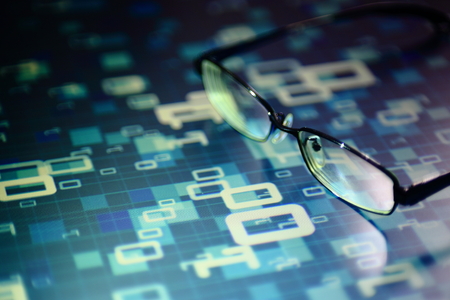 reading data in digital age. glasses and flowing binary code matrix. shallow depth of field image of glasses on display panel. multiple lines of blue code moving under glasses.の写真素材