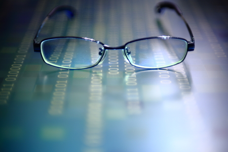 big data analysis. glasses placed on a LED digital panel display white light one and zero binary text number in moving motion pattern. modern technology blue block grid pattern backgroundsの写真素材