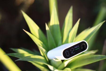measuring outdoors air quality. particulate matter 2.5 (pm.2.5) sensor in a bush. harmful small dust detector indicated healthy acceptable air quality. blur background of blue green plants.の写真素材