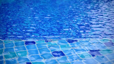 shallow wadding pool water in swimming pool. pool design with small ceramic tiles. repeating dark deep blue tiles dotted lighter shade of blue floor tiles. deeper level in the background.の写真素材