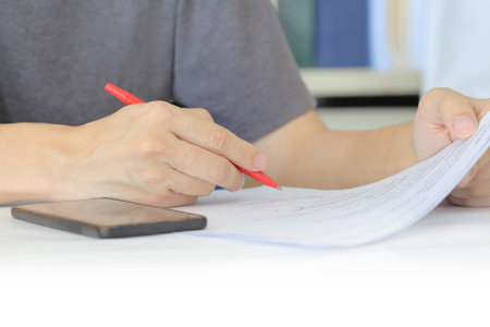 Closeup human hand checking work on a paper. freelance man writing with red pen on paper work. man...