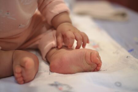 small baby sitting. close up image of baby leg and feet. healthy and happy infant sitting on her own. toddler sat on bed. happy new family concepts.の写真素材