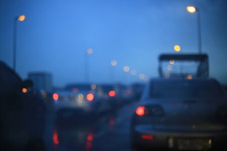out of focus circle light from cars taillight. view from car windshield with rain water droplets foreground reflecting street lamps light. traffic jam due to rain storm. unproductive hour commuting.の写真素材