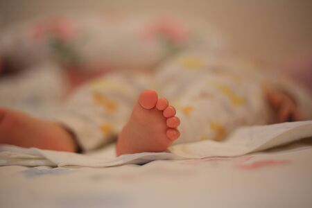 baby laying on the bed. focus on small tiny baby foot. infant sleeping face up. cute girl sleeping soundly. warm and loving family concepts.の写真素材
