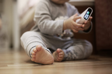 small baby children sitting on bedroom wood floor while holding a air quality sensor. baby learning...