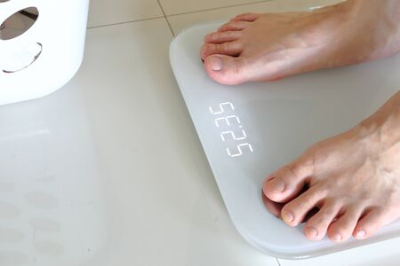 Bare feet standing on a scales. Lose weight concept with person on a scale measuring kilograms. Weight Scale, Underweight man on Scale.の写真素材
