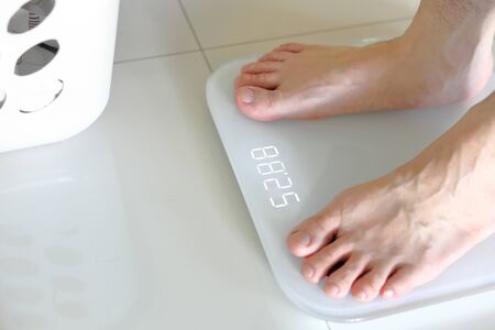 Bare feet standing on a scales. Lose weight concept with person on a scale measuring kilograms. Weight Scale, Underweight man on Scale.の写真素材