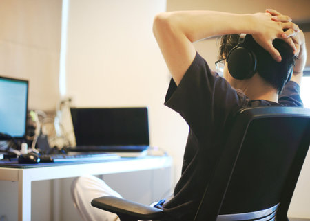 relaxing during work from home. man resting his head on hands while listening music on a headphone while watching computer notebook pc laptop monitor screen.の写真素材