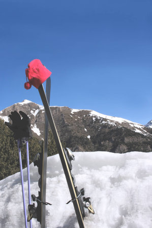 Gloves and hat with skies and poles stuck in the snow with mountain view behindの写真素材