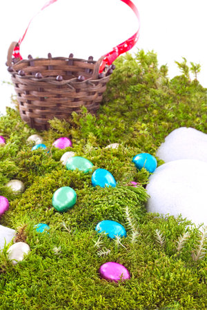 Colored Foil Wrapped Chocolate Easter Eggs On Green Moss Hill with Wicker Basketの写真素材