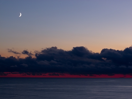 Dramatic sky with dark clouds, red sky and the Moon and Venus in clear sky across English Channel の写真素材