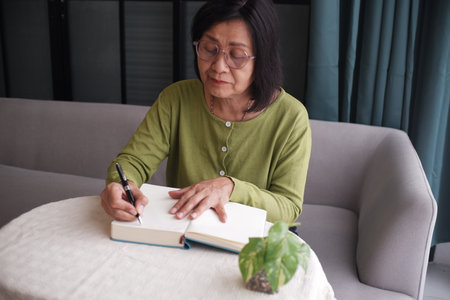 Senior women reading, writing at home, sitting alone on sofa.の写真素材