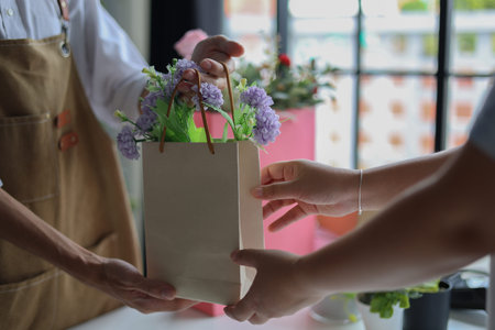 A florist or shop owner, handing a paper bag containing flowers to a customer.Â Flower shop, small...