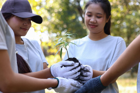 Young adults volunteer planting trees in the park for environmental conservation and sustainable...