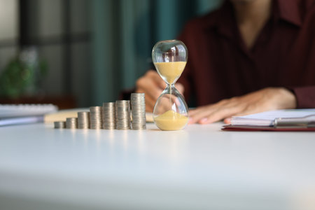 Rising stack of coins and running sand clock on the table. Growing of income, saving or return...