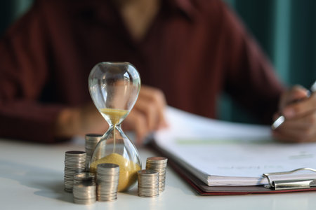Coin stacks and sand clock on the table. Growing of income, saving or return investment through...
