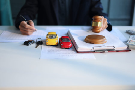 A man working on desk with gavel, contracts, and toy cars. Concept for Car Auction Legalities or...