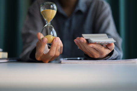 Time and money concept. Businessman holding cash and sand clock imply growth of income, saving or return investment through time.の写真素材