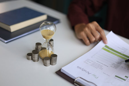 Coin stacks and sand clock on the table. Growing of income, saving or return investment through...