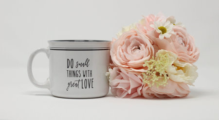 inspirational message on a coffee or tea mug next to pastel bouquet of flowers on a white background