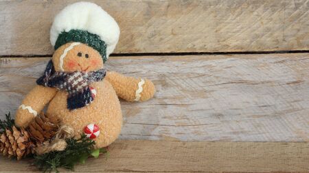 stuffed gingerbread man with fluffy chef hat cloth scarf and candy button standing on a wood background with copy spaceの写真素材
