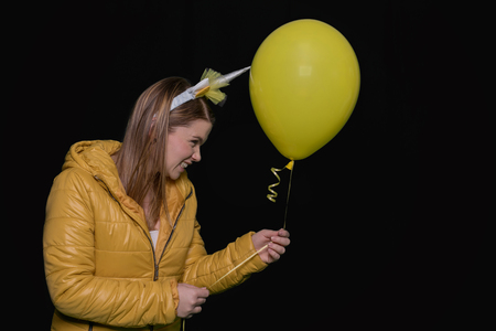Beautiful young woman with unicorn horn and balloon on black backgroundの写真素材