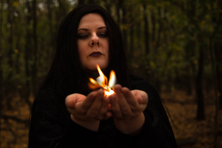 Black-haired witch holds fire in her hands in the forest.の写真素材